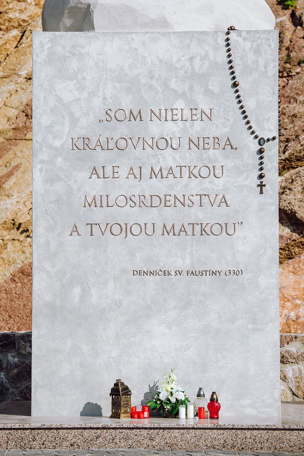 Celý nápis o Márii ako Matke milosrdenstva a ruženec na podstavci sochy